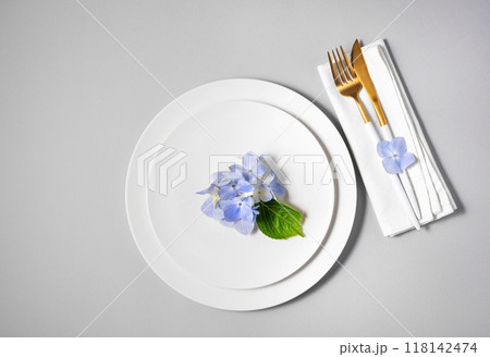 Festive table setting with blue hydrangea flowers on white plates and a napkin with cutlery Festive table setting with blue hydrangea flowers on white plates and a napkin with cutlery 118142474