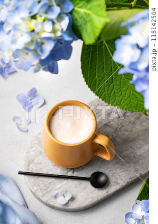 Spring bouquet with blue hydrangea flowers and a cup of cappuccino coffee in a yellow cup and spoon on a light background. The concept of a morning drink for breakfast. 118142504