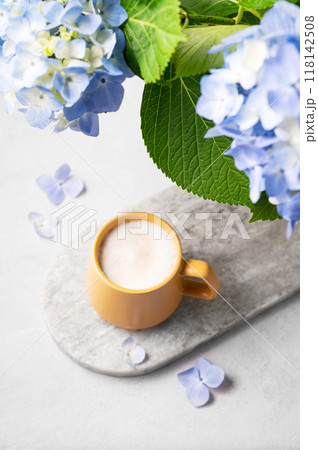 Spring bouquet with blue hydrangea flowers and a cup of cappuccino coffee in a yellow cup Spring bouquet with blue hydrangea flowers and a cup of cappuccino coffee in a yellow cup 118142508