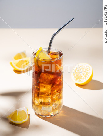 Iced tea with lemon and ice in a tall glass on a yellow background with shadow and fruits. Iced tea with lemon and ice in a tall glass on a yellow background with shadow and fruits. 118142795