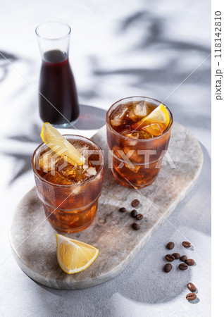 Cold brew coffee in a two glasses with lemon and ice on a marble board on a light background  118142810
