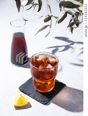 Cold brew coffee in a glass with ice on a light background with lemon fruit, bottle and branch Cold brew coffee in a glass with ice on a light background with lemon fruit, bottle and branch 118142821