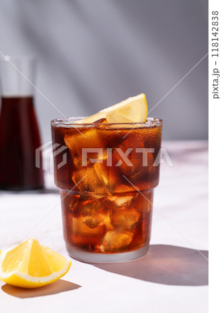 Cold brew coffee in a glass with ice and lemon on a light marble background with bottle and shadows Cold brew coffee in a glass with ice and lemon on a light marble background with bottle and shadows 118142838