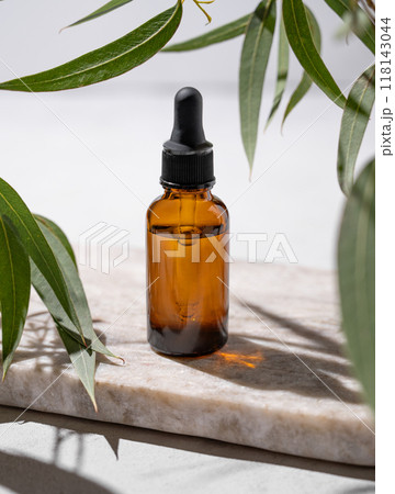 Face and body serum in bottle on a marble board on a white background with green leaves and shadow. Face and body serum in bottle on a marble board on a white background with green leaves and shadow. 118143044