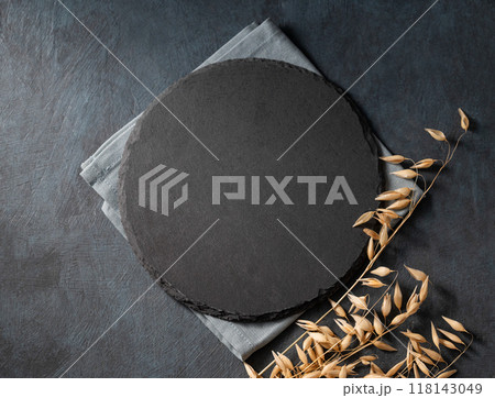 Round slate empty board on a dark background with golden stalks of wheat. 118143049