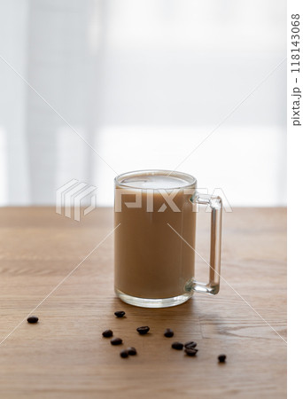 A cup of coffee with milk on a wooden table with coffee beans against the background of a window. 118143068