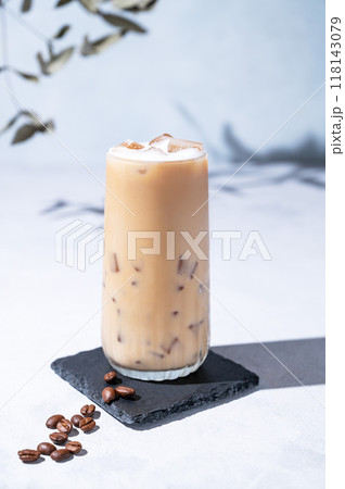 Iced coffee latte in a tall glass with milk on a light background with coffee beans 118143079