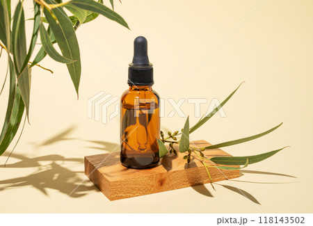 Face and body serum in bottle on a wooden board on a yellow background with green leaves and shadow. 118143502