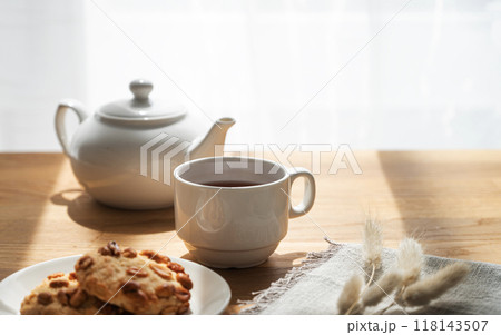 A cup of tea with homemade cookies and a white teapot on a wooden table against the background  118143507