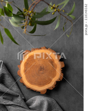 Wooden empty round board with green leaves and napkin on a dark gray background. Wooden empty round board with green leaves and napkin on a dark gray background. 118148182