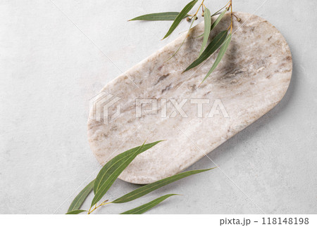 Empty marble board or tray with green leaves on a light texture  background. Empty marble board or tray with green leaves on a light texture  background. 118148198
