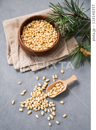 Pine nuts in a bowl  and a scattered on a blue background with branches of pine needles.  118148357