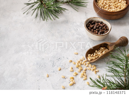 Flat lay of pine nuts in a bowl and wooden scoop on a light texture background with branches  118148371