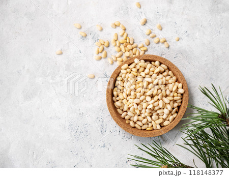 Pine nuts in a  wooden plate and scattered on a light texture background with branches  118148377