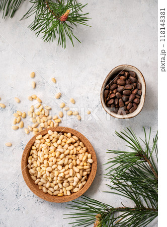 Pine nuts in a bowl and scattered on a white texture background with branches of pine needles. Pine nuts in a bowl and scattered on a white texture background with branches of pine needles. 118148381