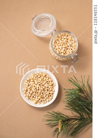 Pine nuts in a bowl and jar on a yellow background with branches of pine needles. 118148551