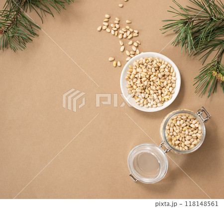 Pine nuts in a white plate and a jar on a yellow background with branches of pine needles  118148561