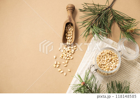 Pine nuts in a jar and wooden scoop on a yellow background with branches of pine needles. Pine nuts in a jar and wooden scoop on a yellow background with branches of pine needles. 118148585