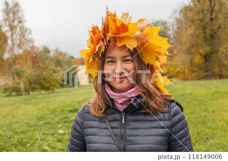Happy smiling woman in yellow leaves wreath outdoor on autumn background, portrait 118149006