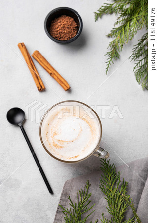 Spiced coffee latte or cappuccino with cinnamon sticks on a light background with fir branches. Spiced coffee latte or cappuccino with cinnamon sticks on a light background with fir branches. 118149176
