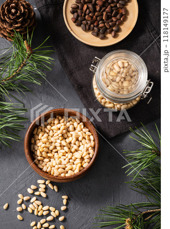 Pine nuts in a jar, bowl and a scattered on a dark background with branches of pine needles and cone Pine nuts in a jar, bowl and a scattered on a dark background with branches of pine needles and cone 118149177