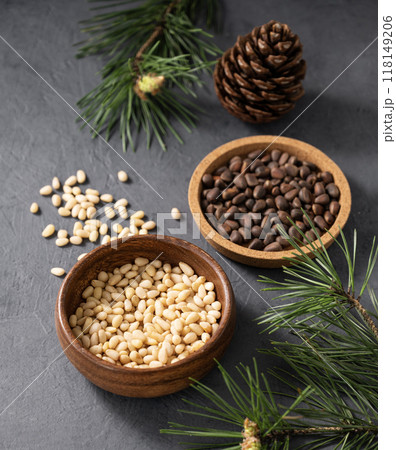 Pine nuts in a wooden bowl and scattered on a dark background with branches of pine needles. 118149206