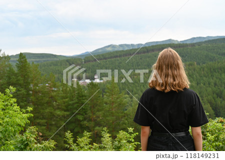 View from the back of young hiker girl wearing backpack and beanie hat standing on edge of cliff and enjoying landscape, sunset, mountains and clouds. 118149231