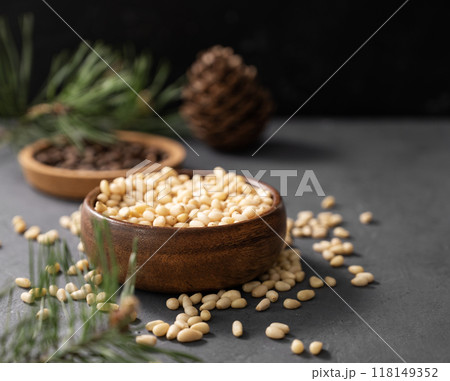 Pine nuts in a bowl and a handful of unpeeled nuts on a gray background with a branch Pine nuts in a bowl and a handful of unpeeled nuts on a gray background with a branch 118149352