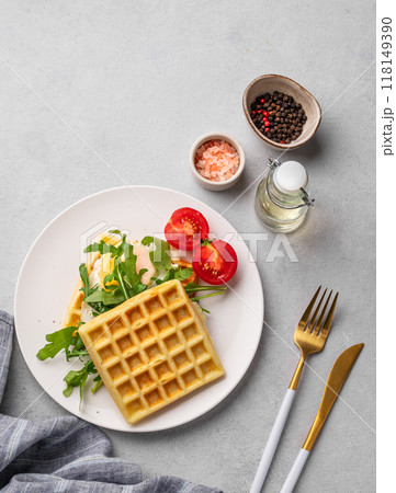 Waffles with fried egg, cherry tomatoes and arugula on a white plate on a gray texture background 118149390