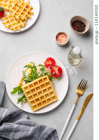 Waffles with fried egg, cherry tomatoes and arugula on a white plate on a gray texture background  118149393
