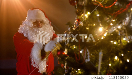 Santa Claus decorates the Christmas tree. Santa claus putting presents under the tree. Santa Claus near the Christmas tree. 118150029