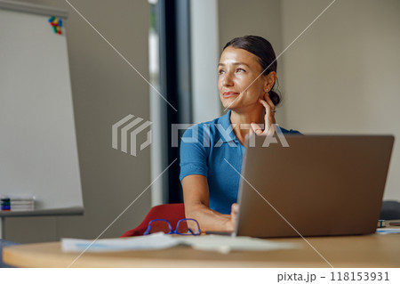 A Thoughtful Professional Woman Engaged in Work on Laptop Inside a Modern Office Space 118153931