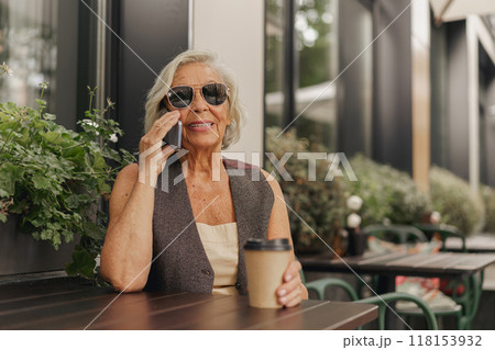 A Stylish Senior Woman Happily Enjoying Her Coffee at a Charming Outdoor Cafe Space 118153932