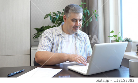 A man works on a computer. He looks at the screen and types on the keyboard. Perfect for content about remote work, freelancing and office work. 118155382