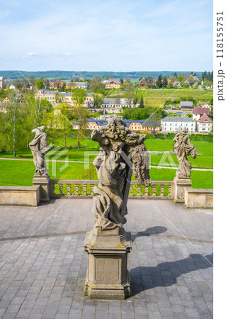 Baroque statues stand elegantly within the gardens of Kuks hospital complex, overlooking lush greenery and quaint buildings in the distance, creating a serene atmosphere. Baroque statues stand elegantly within the gardens of Kuks hospital complex, overlooking lush greenery and quaint buildings in the distance, creating a serene atmosphere. 118155751