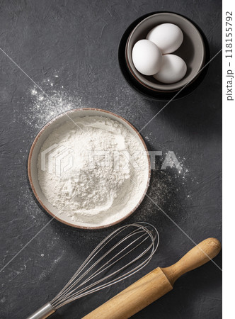 Natural organic flour in a bowl with a eggs and rolling pin on a dark gray background. Natural organic flour in a bowl with a eggs and rolling pin on a dark gray background. 118155792