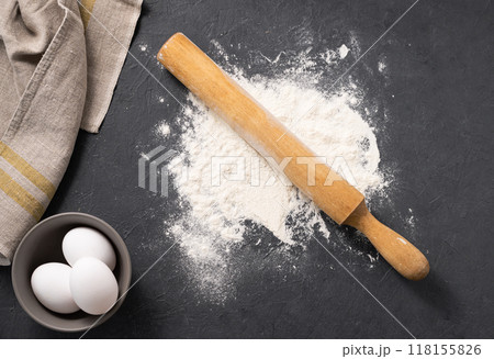 Natural wheat flour is scattered on a dark background with eggs and napkin. Natural wheat flour is scattered on a dark background with eggs and napkin. 118155826