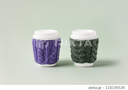 Two cups made of cardboard for takeaway coffee with knitted green and purple cover and white bioplastic lid. Concept of takeaway coffee, walking, energetic life Two cups made of cardboard for takeaway coffee with knitted green and purple cover and white bioplastic lid. Concept of takeaway coffee, walking, energetic life 118156526