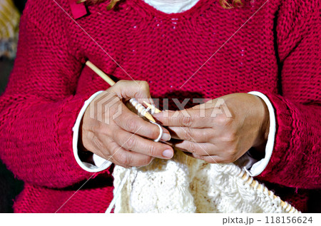 Close-up of woman in red sweater knitting white wool yarn with needles by hand 118156624