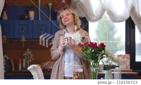 Cute blonde in the kitchen, drinking morning coffee. She holds a mug with a hot drink in her hands. A woman living alone enjoys a peaceful day off. 118156723