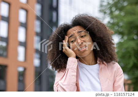 Portrait of a young woman in an urban setting experiencing a headache, showing discomfort and stress while holding her head. 118157124