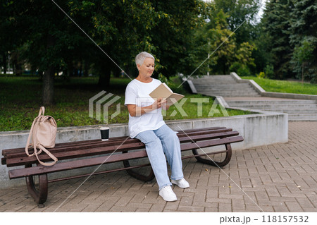 Full length portrait of older woman with short gray hair reading paper book in park, enjoying nature and tranquility, embodying relaxation and wisdom. Elderly female enjoying free time in retirement. 118157532