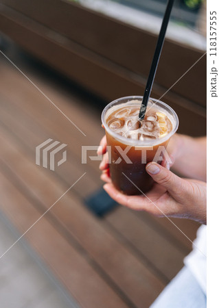 Vertical cropped shot of unrecognizable female tourist holding ice beverage drink during walking on city street. Woman drinking iced coffee through straw, enjoying free time in travel. Vertical cropped shot of unrecognizable female tourist holding ice beverage drink during walking on city street. Woman drinking iced coffee through straw, enjoying free time in travel. 118157555