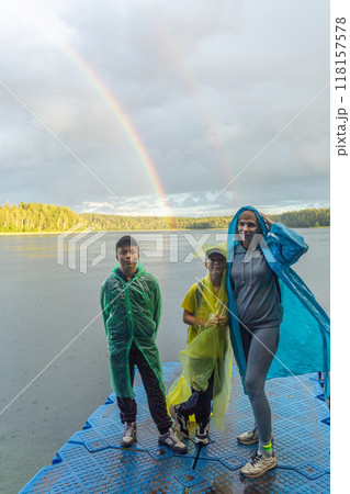 Family in raincoats enjoy a lakeside view with a vivid rainbow in the background. Family in raincoats enjoy a lakeside view with a vivid rainbow in the background. 118157578