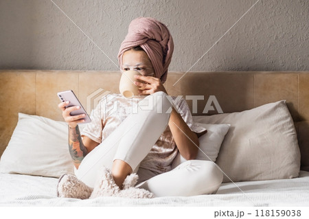 Woman with towel on head drinking coffee and reading phone in bed. Woman with towel on head drinking coffee and reading phone in bed. 118159038