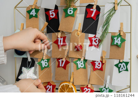 Number on craft paper notes with tasks before Christmas holidays. Female making kraft paper for handmade advent calendar Made with your own hands step by step DIY 118161244