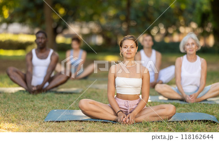 Multinational yoga enthusiasts with female coach perform Baddha konasana in park 118162644
