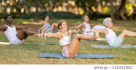 Athletic men and women of different nationalities warm up together before doing yoga in summer park 118162882