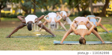 Girl performing Prasarita Padottanasana with group during yoga class in park 118162898