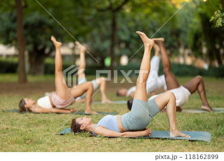 Woman doing One Legged Bridge Pose during group yoga in park 118162899